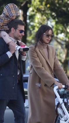 a man and woman walking with a baby on their back while holding onto the handlebars of a bicycle