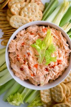 a white bowl filled with tuna salad next to crackers and celery sticks