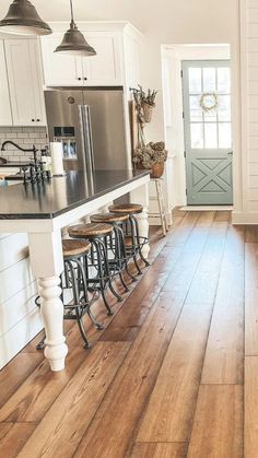 a kitchen with wooden floors and white cabinets, an island countertop and stools