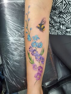 a woman's arm with flowers and a bee on it, while she is sitting down