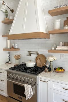 a stove top oven sitting inside of a kitchen next to wooden shelves and white cabinets