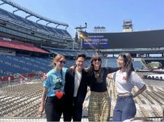 three women and one man are posing for a photo in front of the bleachers