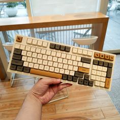 a hand holding a wooden keyboard in front of a table