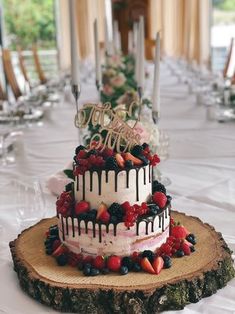 a three tiered cake with berries and strawberries on the top is sitting on a wooden slice