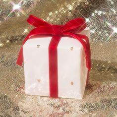 a white gift box with a red bow on it sitting on a gold sequin background