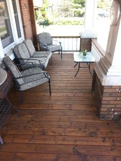 two chairs and a table on a wooden porch with brick pillars, glass tables and windows