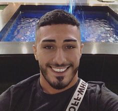 a man with a ribbon around his neck smiles at the camera in front of a fountain