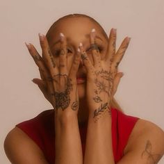 a woman covering her face with both hands and covered by tattoos on her arms, in front of a white wall