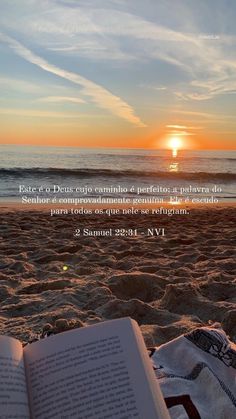 an open book sitting on top of a sandy beach next to the ocean at sunset