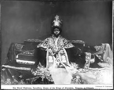 an old black and white photo of a woman dressed in elaborately designed clothing, sitting on a table