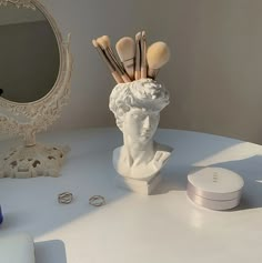 there is a statue with makeup brushes in it on the table next to a mirror