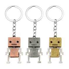 three metal robot keychains are shown in different colors and sizes, one is silver, the other is gold