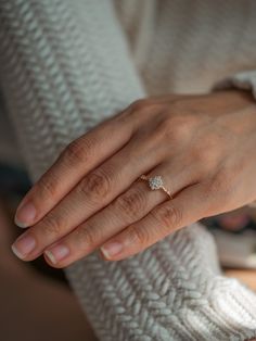 a woman's hand with a diamond ring on her left hand, wearing a white sweater