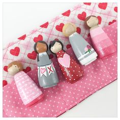 three wooden peg dolls sitting on top of a pink mat next to hearts and polka dots