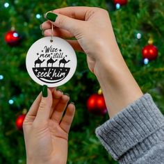 a person holding up a christmas ornament in front of a christmas tree