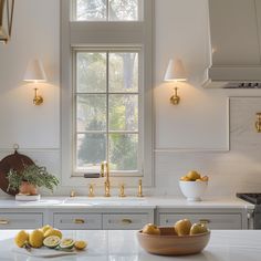 a white kitchen with gold accents and marble counter tops is pictured in this image, there are lemons on the counter