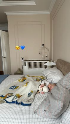 a baby is laying in bed under a blanket and holding a stuffed animal while looking at the camera