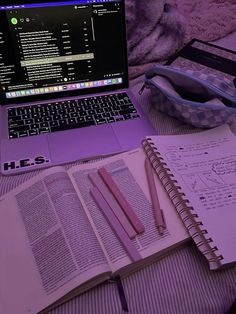 an open laptop computer sitting on top of a bed next to a notebook and pen