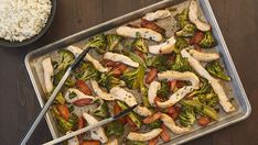 chicken and broccoli stir fry in a pan with rice next to it on a wooden table