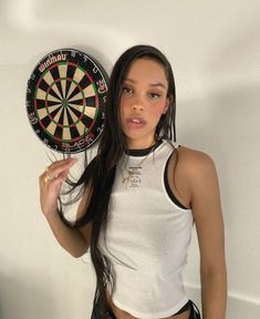 a woman holding up a dart and a darts board