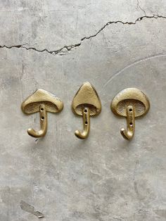 three brass door handles with mushrooms on them against a concrete wall, one has a letter t and the other is a mushroom