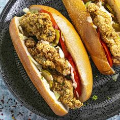 two sandwiches with meat and vegetables on a black plate next to some breaded buns