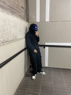 a man in a hoodie leaning against a wall talking on a cell phone