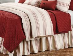 a bed with red and white bedspreads, pillows and blankets on top of it