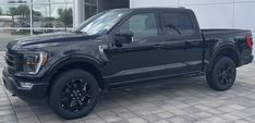 a black ford f - 150 pickup truck parked in front of a dealers showroom