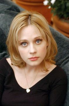 a close up of a person sitting on a couch wearing a black shirt and gold necklace