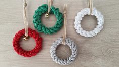 four different colored crocheted rings hanging from strings on a wooden surface with gold bells