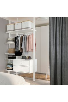 a white closet with clothes hanging on the shelves and drawers in front of a bed