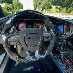 the interior of a sports car with its steering wheel and dash lights on, in front of some trees