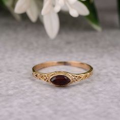 a close up of a gold ring with a garnet stone in the middle and flowers behind it