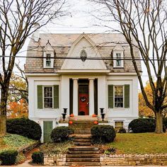 a white house with green shutters and steps leading up to the front door is surrounded by trees