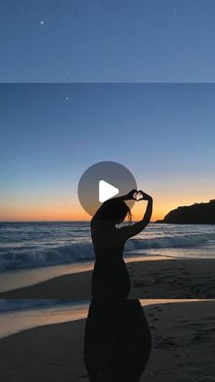 a woman standing on top of a beach next to the ocean at sunset with her reflection in the water