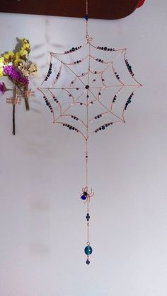 a spider web hanging from the ceiling with beads and flowers on it's side