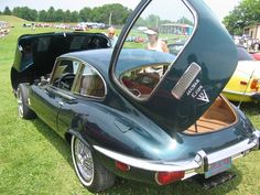 an old car parked in the grass with its door open and people looking at it