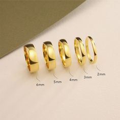 four different sizes of gold wedding rings on a white surface with measurements for each ring