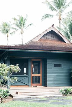 a house that is painted blue and has palm trees in the front yard behind it