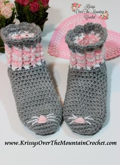 a pair of crocheted gray and pink baby booties next to a bouquet of flowers