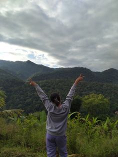 a person standing on top of a lush green hillside with their arms in the air