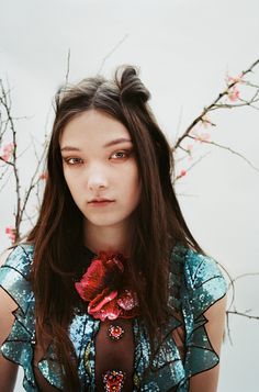 a woman with long hair wearing a flower in her lap and looking at the camera