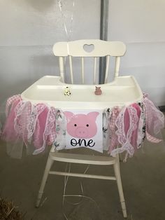 a white chair with pink ruffles and a one year old sign on it