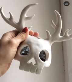 a hand holding a white skull with antlers on it's head and eyes