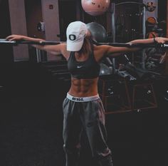 a woman is doing exercises with a barbell in the gym while wearing a hat