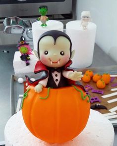 there is a cake decorated like a little dracula on top of a pumpkin with other halloween decorations around it