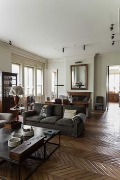 a living room filled with lots of furniture and wooden flooring next to tall windows