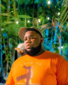 a man wearing an orange shirt and hat standing in front of some trees at night