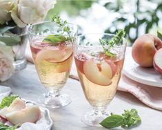 two wine glasses filled with peaches and mint garnish sitting on a table